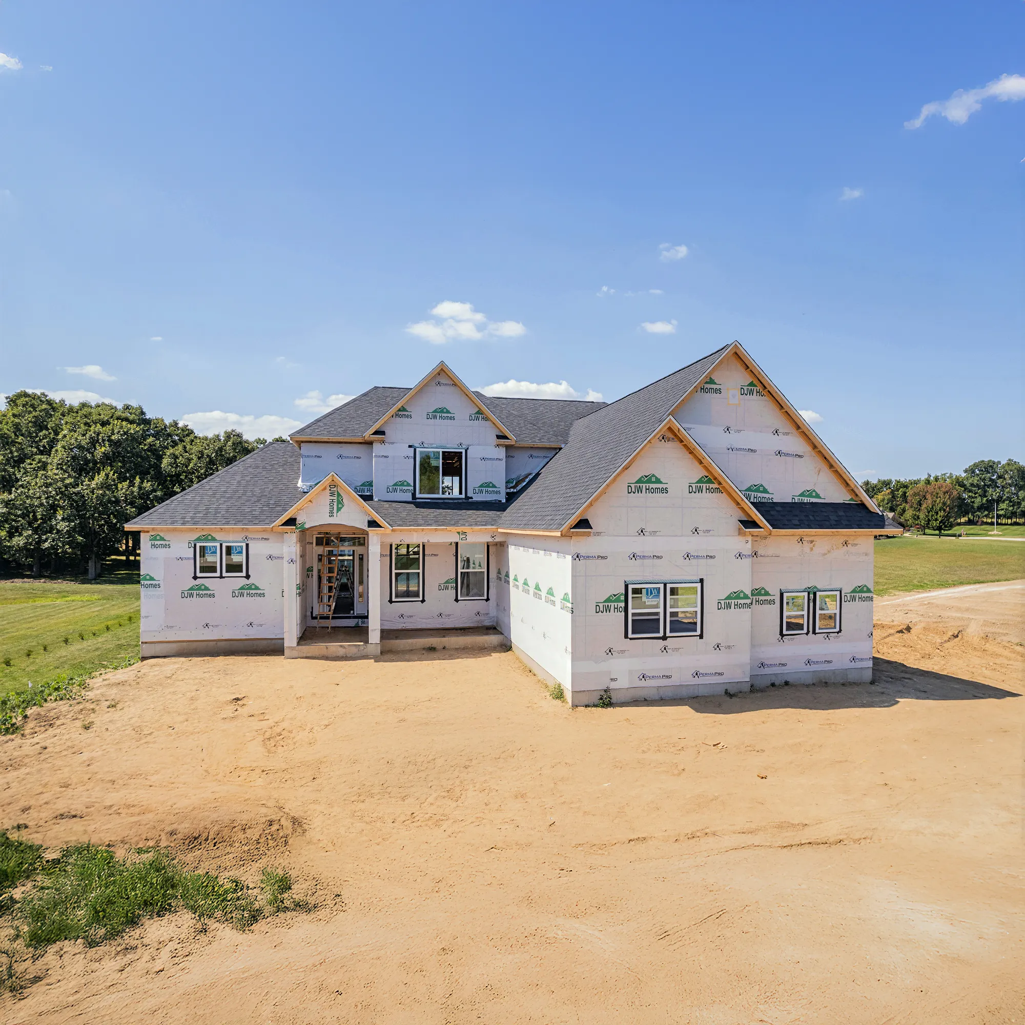 A closer look at this two-story house in Adrian, Michigan shows it is nearly complete, surrounded by greenery, and awaiting its final exterior finishes. With a multi-gabled roof and many windows, the home highlights a bright, open design in a peaceful setting.